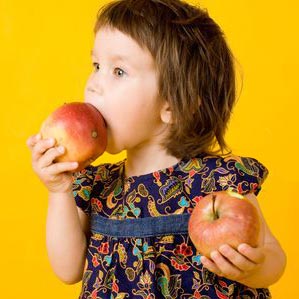 دختر کوچولو با دو سیب گاز زده در دو دست 