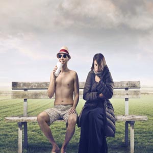زن و مرد بر روی نیمکت در چمنزار مرد با لباس تابستانی و زن با لباس زمستانی